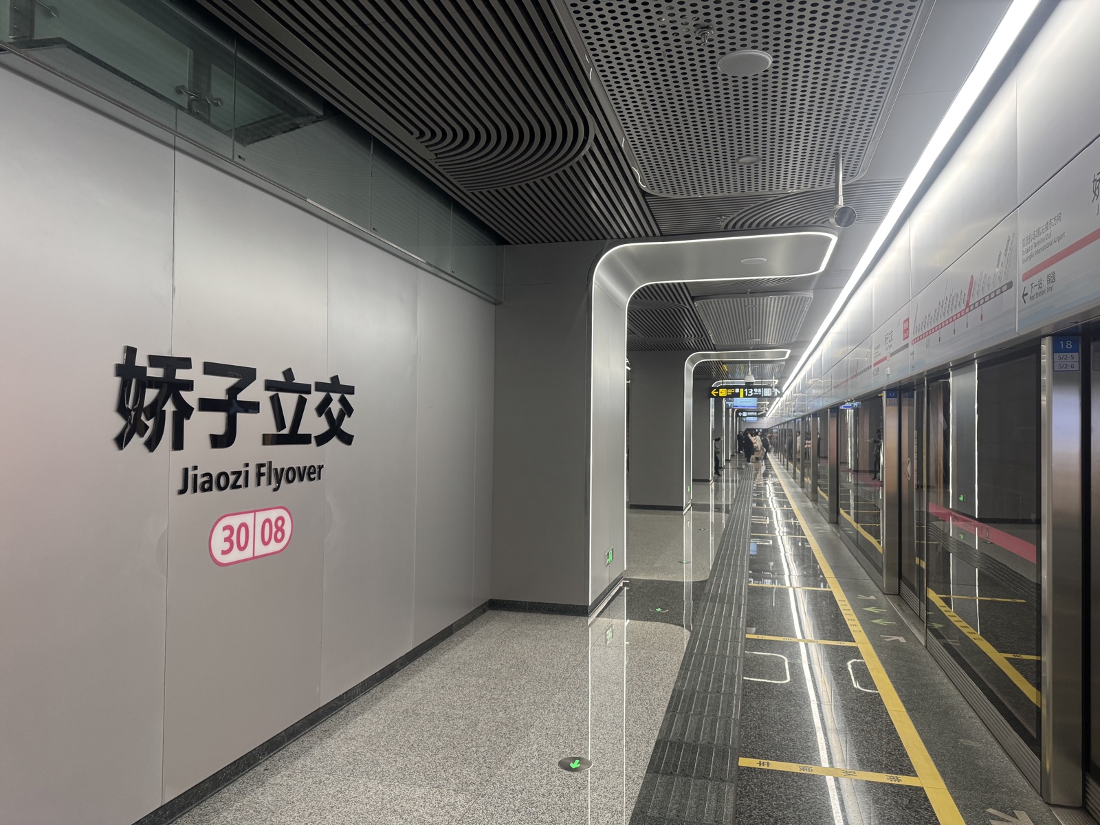 Andén de la estación Jiaozi Flyover de Chengdu, con el nombre de la estación en dos idiomas, puertas de vidrio y pasajeros al fondo.