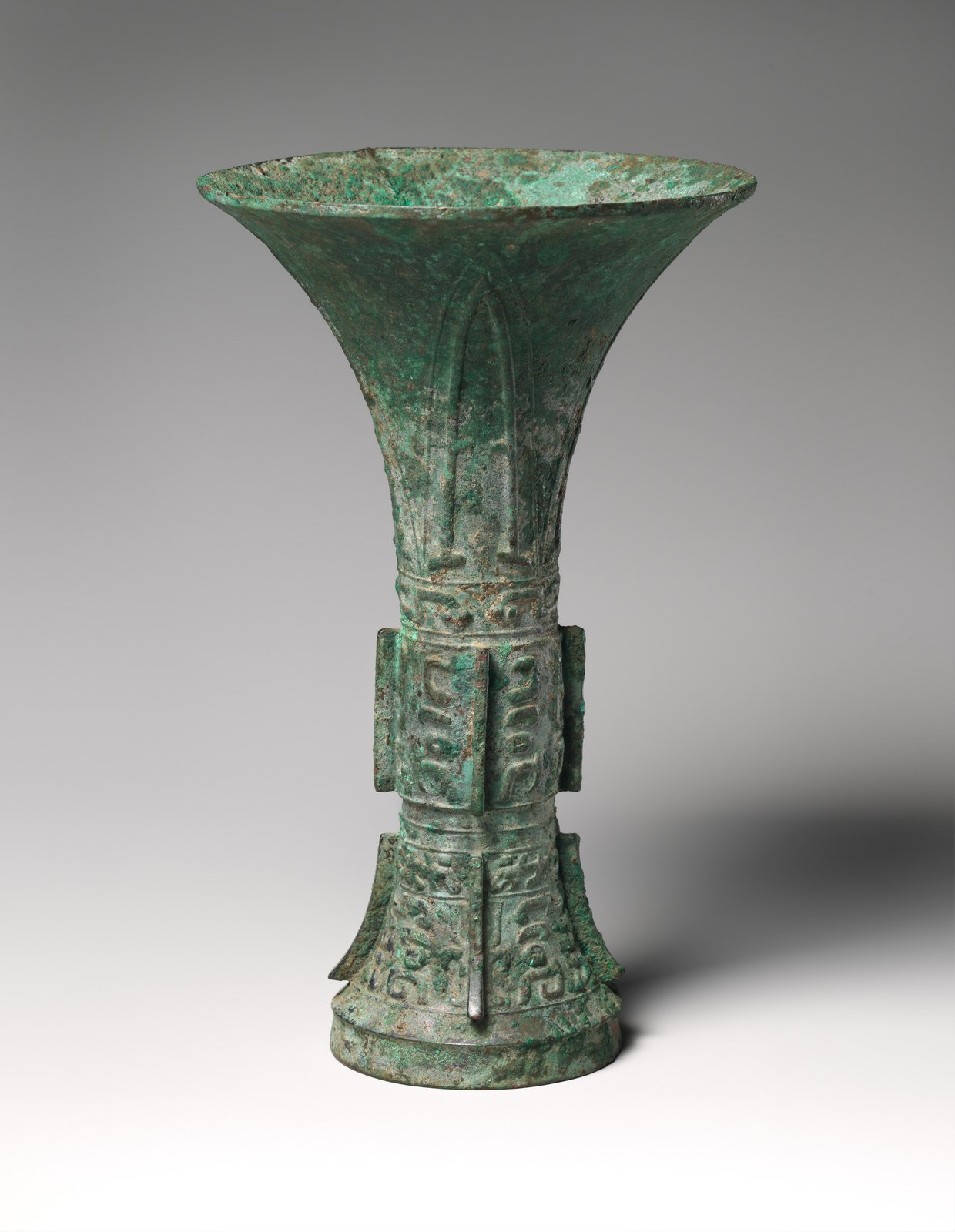 Tall green-patinated bronze gu beaker with a flared mouth, narrow waist and vertical ridges