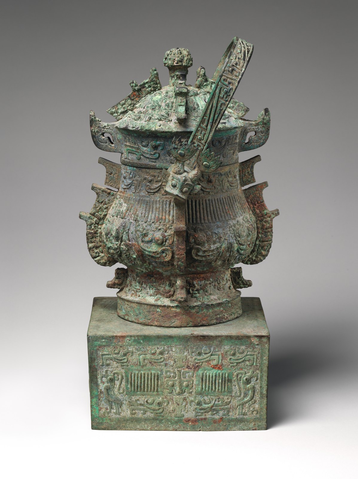 Lidded bronze wine container with an arched handle and projecting ornament on a rectangular support