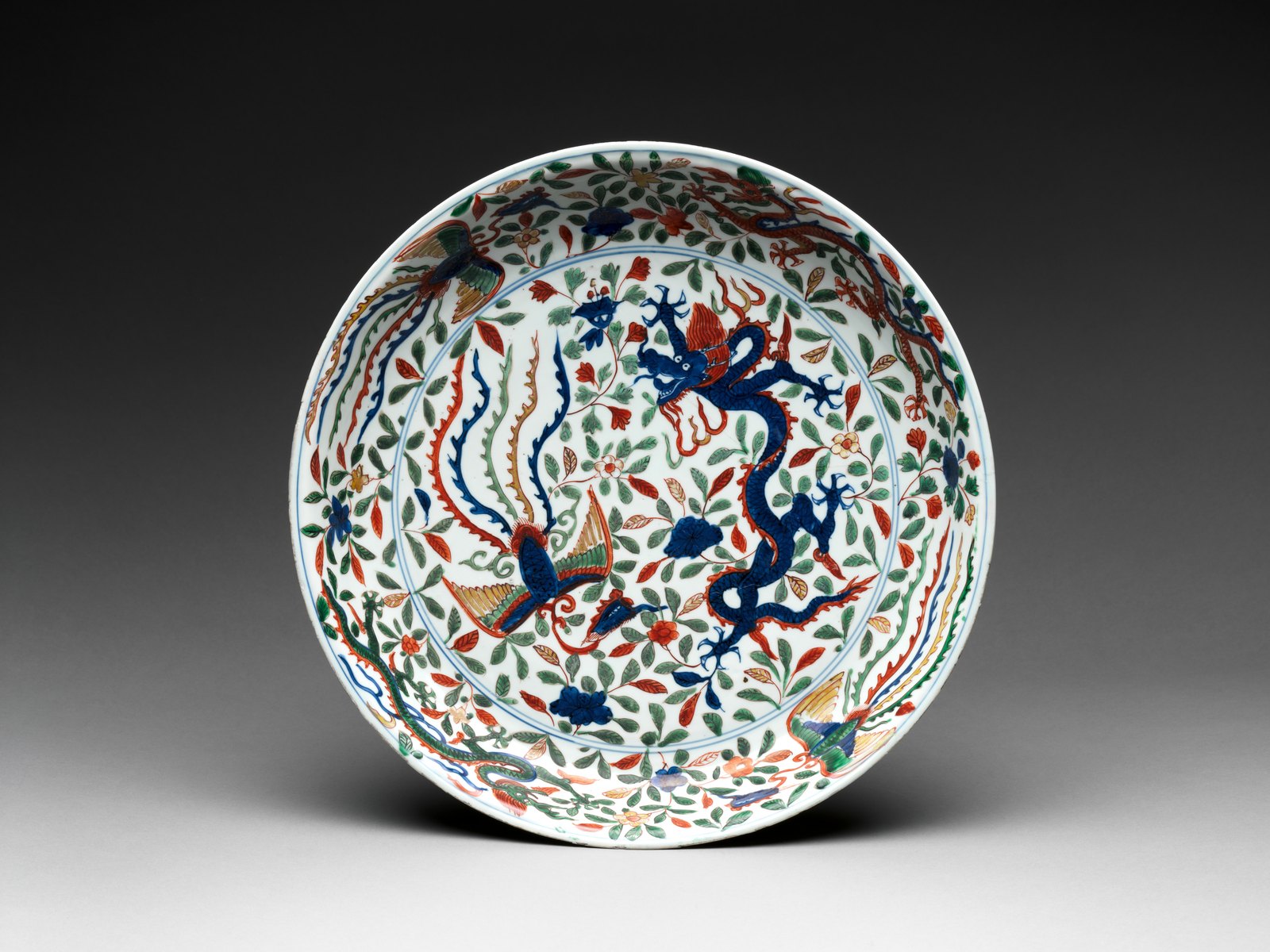 Polychrome porcelain dish displayed upright with a five-clawed blue dragon and a long-tailed fenghuang among flowering vines