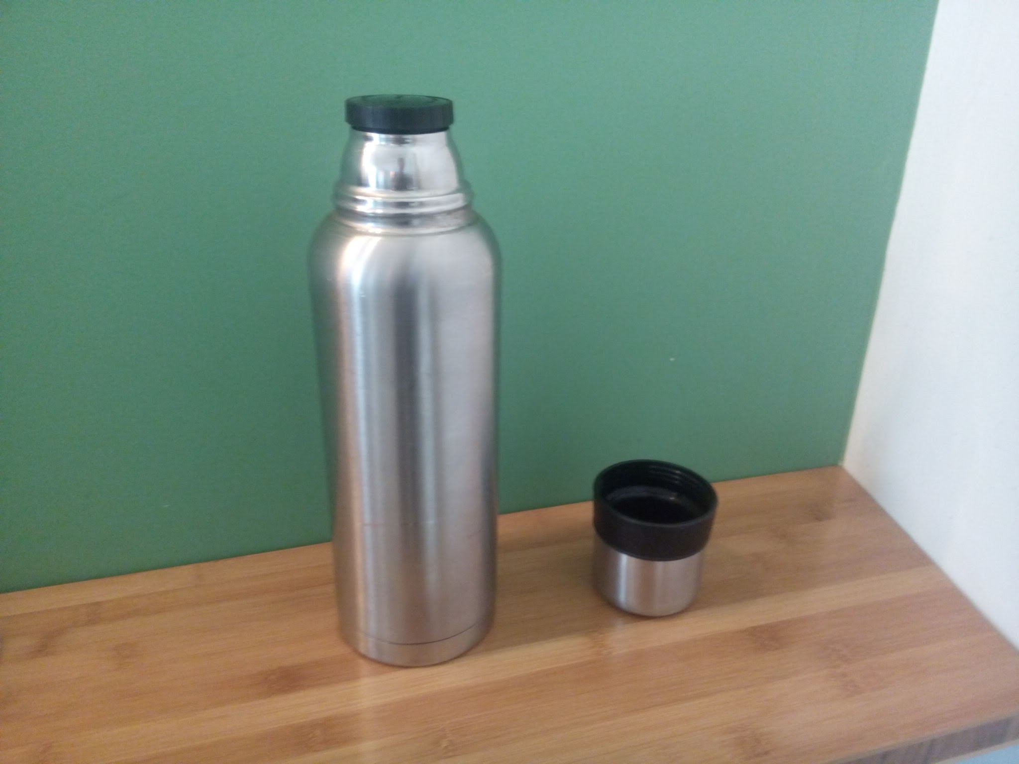 Open vacuum flask beside a cup of hot water.