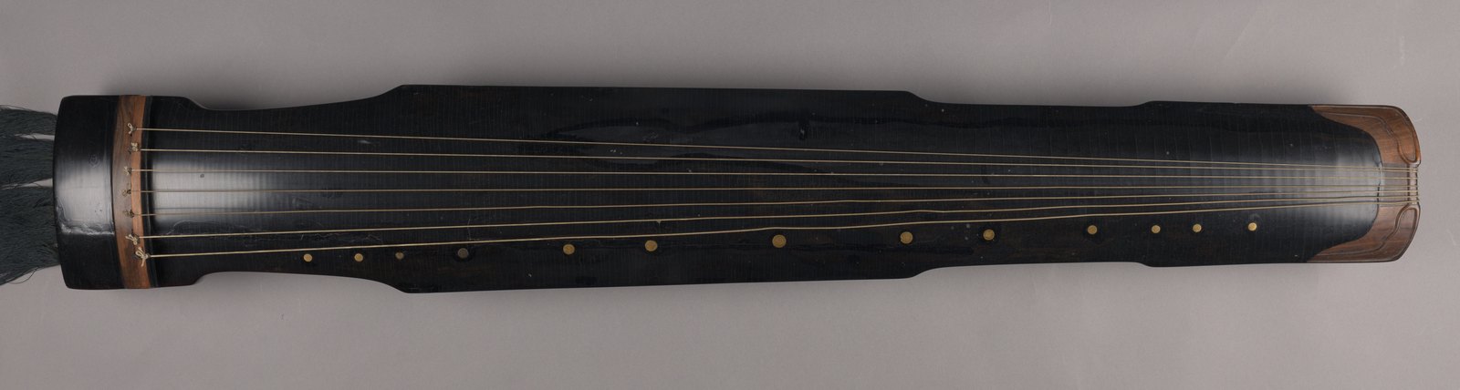 Elongated dark lacquered qin with seven strings running along its body.