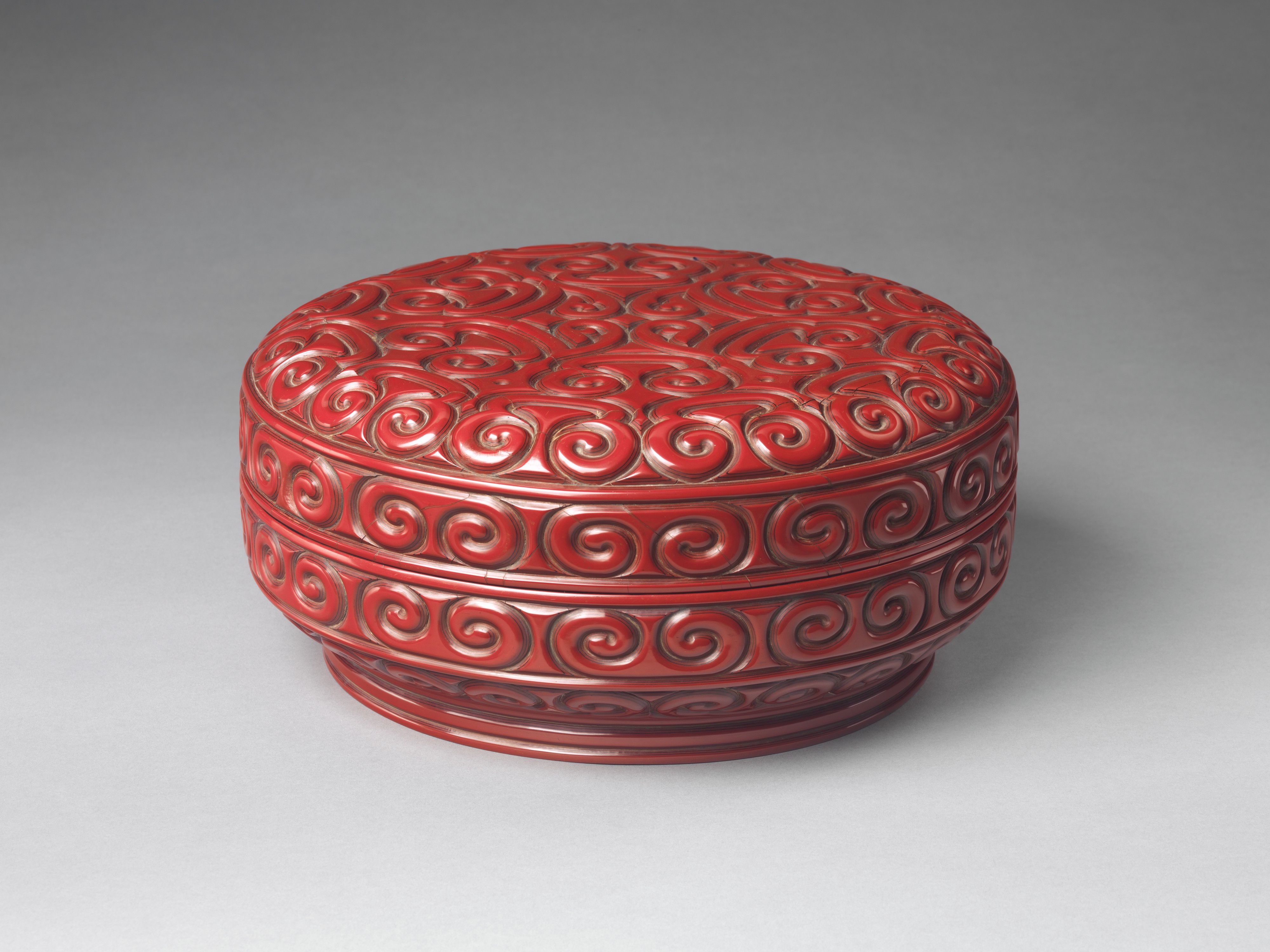 Layered red and black lacquer carved into a dense scroll pattern.