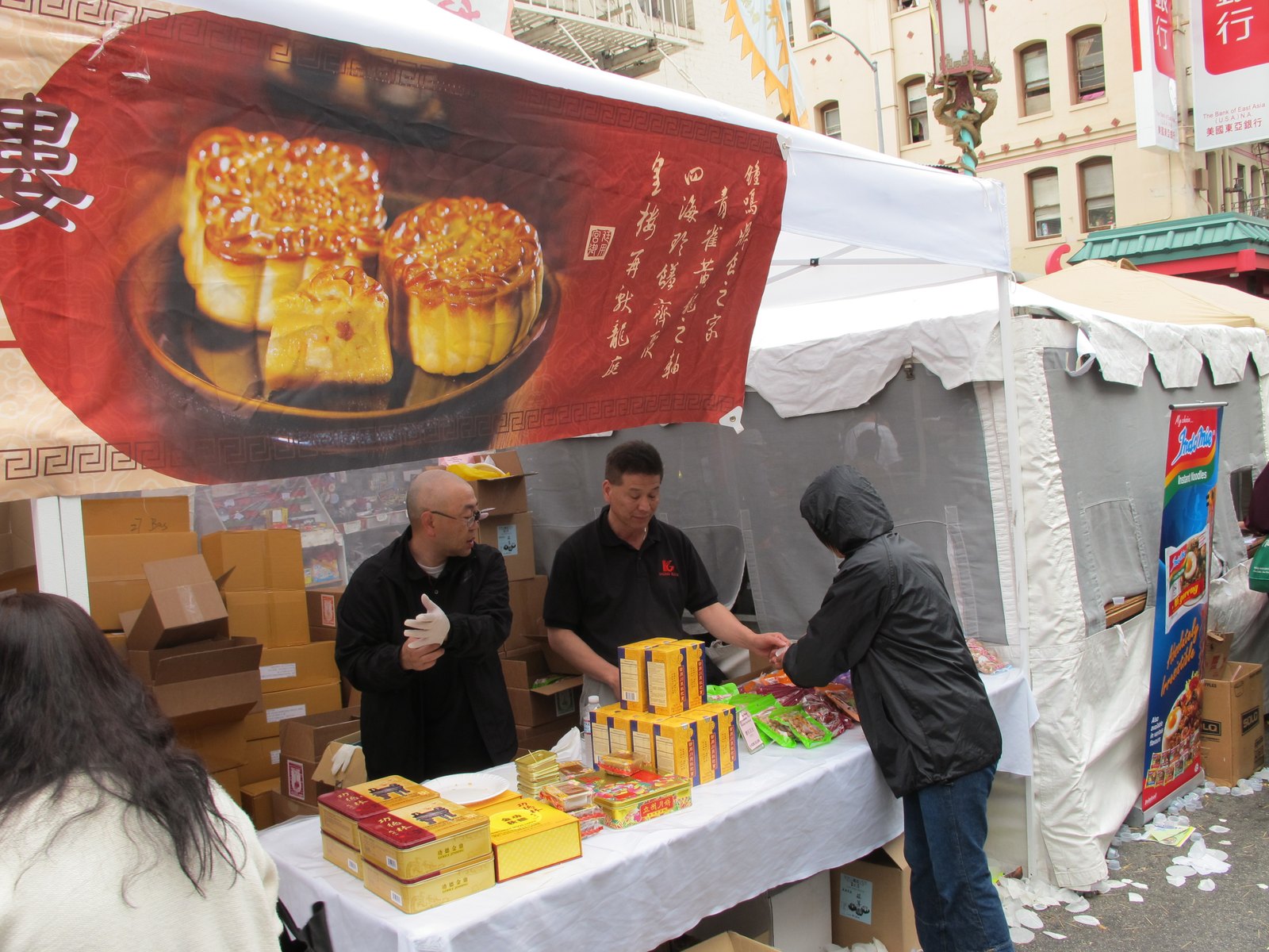 Vendors serve a customer behind boxes of mooncakes at an outdoor stall in San Francisco Chinatown.