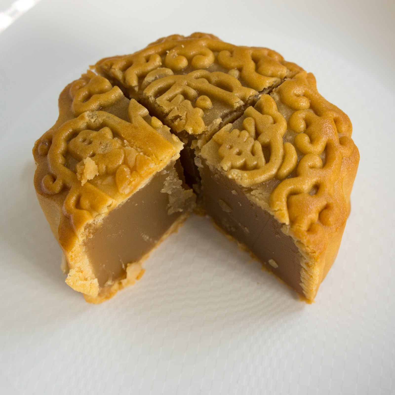 A cut lotus-paste mooncake showing its crust and filling