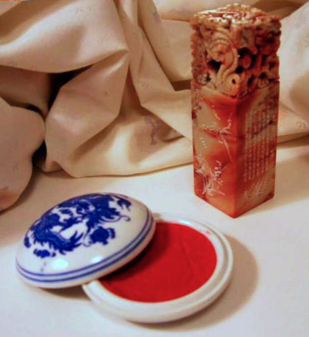 A carved Chinese seal rests beside the red paste used to make an impression.