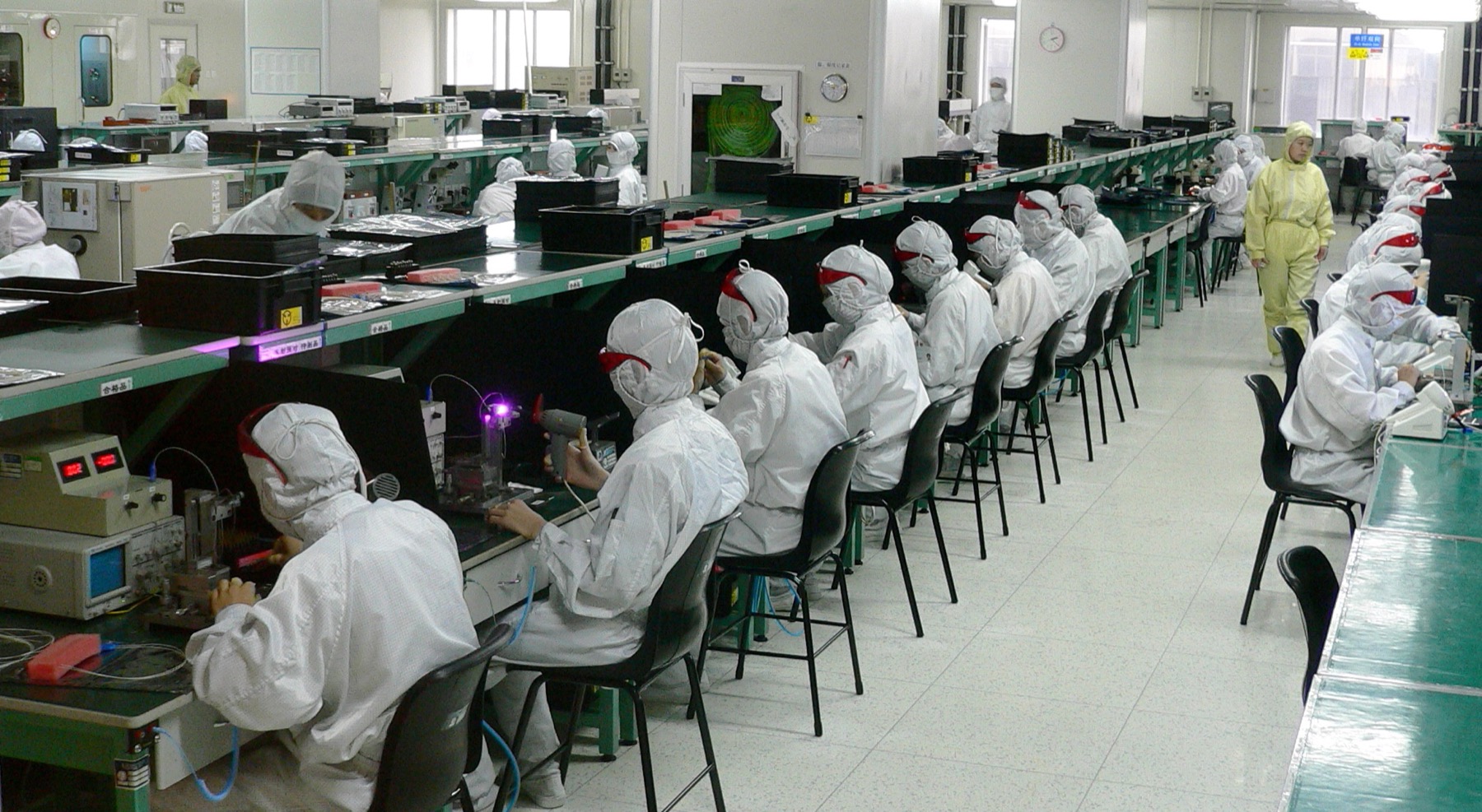 Workers in protective clothing seated along electronics workbenches in a Shenzhen factory