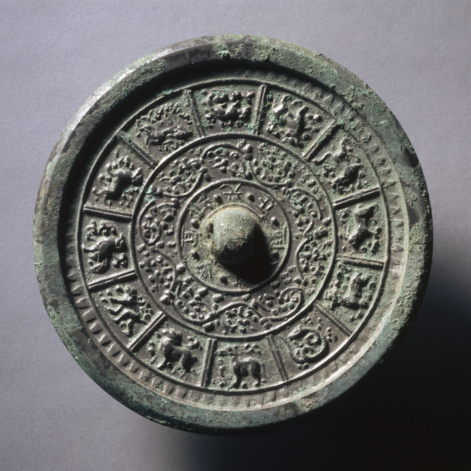 Twelve zodiac animals circle a Sui-dynasty bronze mirror among interlaced floral motifs.